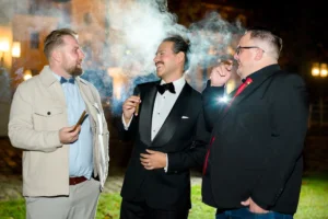 Esküvő fotózás külföldön - Party - színes esküvői kép a vőlegényről és a barátairól szivarozás közben.