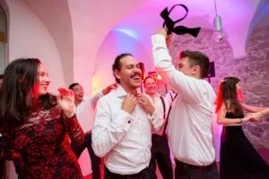 Esküvő fotózás külföldön - Party - vicces színes kép a vőlegényről és barátairól, ahogy leveszik Ricardo nyakkendőjét tánc közben.